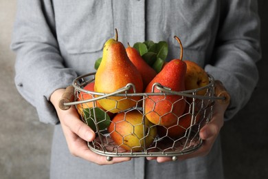 Photo of Woman holding metal basket with ripe juicy pears indoors, closeup