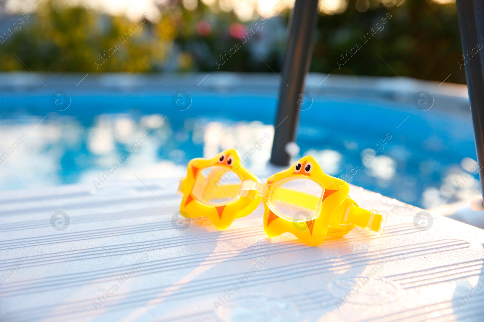 Photo of Yellow swimming goggles for kids on ladder outdoors, closeup. Space for text