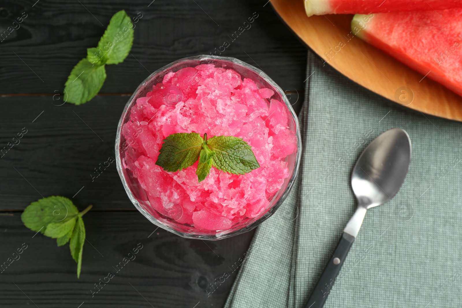 Photo of Tasty watermelon sorbet with mint in glass dessert bowl and spoon on black wooden table, flat lay