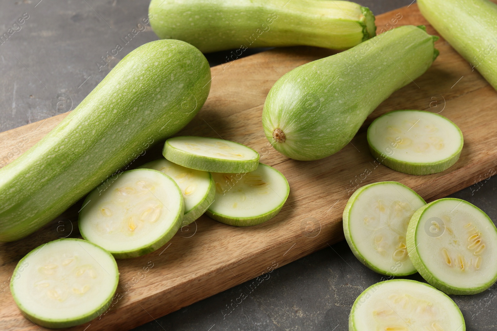 Photo of Board with fresh cut and whole zucchinis on grey textured table, closeup