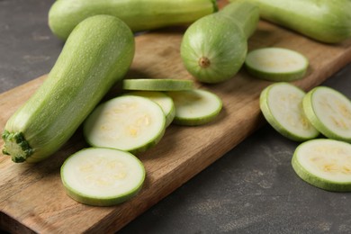 Photo of Board with fresh cut and whole zucchinis on grey textured table, closeup