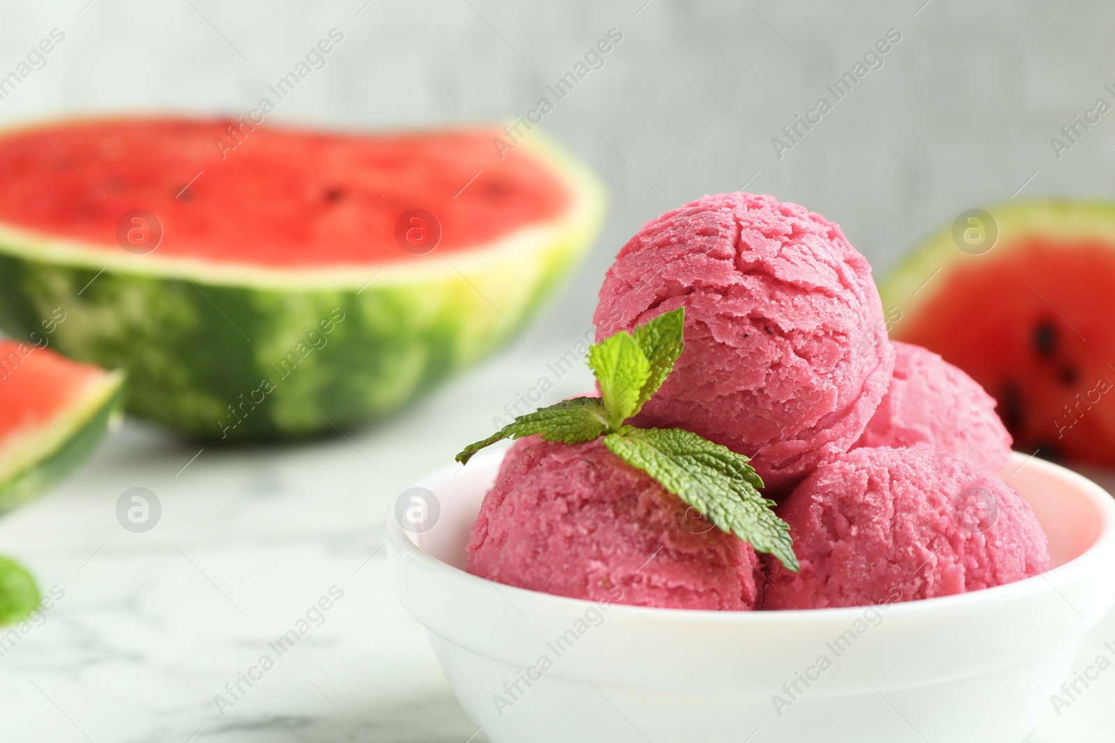 Photo of Scoops of tasty watermelon sorbet with mint in bowl on white table, closeup