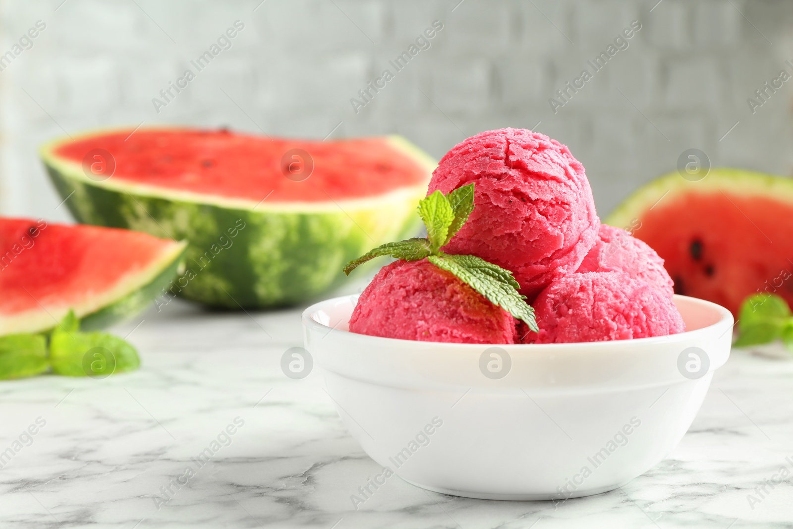 Photo of Scoops of tasty watermelon sorbet with mint in bowl on white marble table, closeup. Space for text