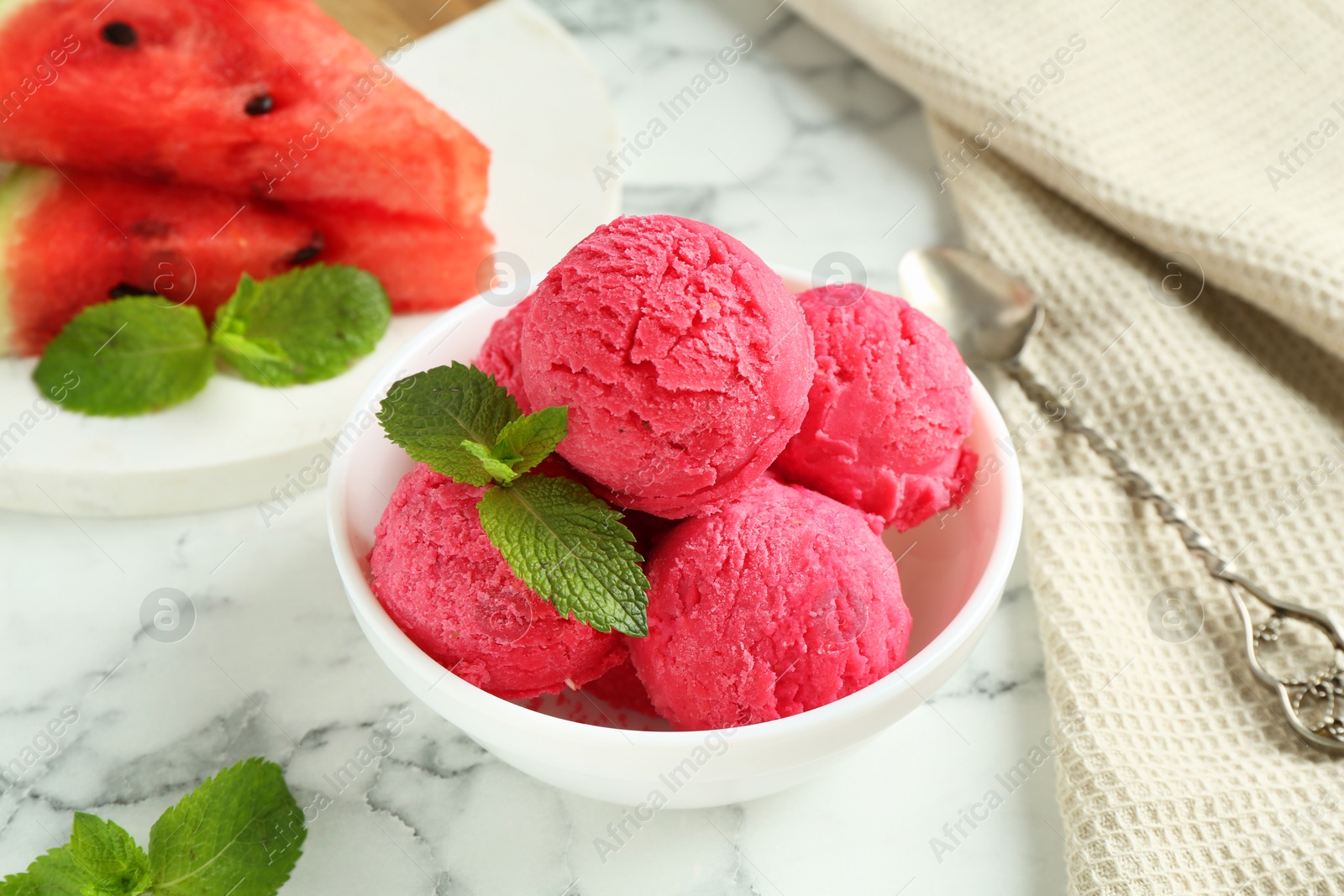 Photo of Scoops of tasty watermelon sorbet with mint in bowl on white marble table, closeup