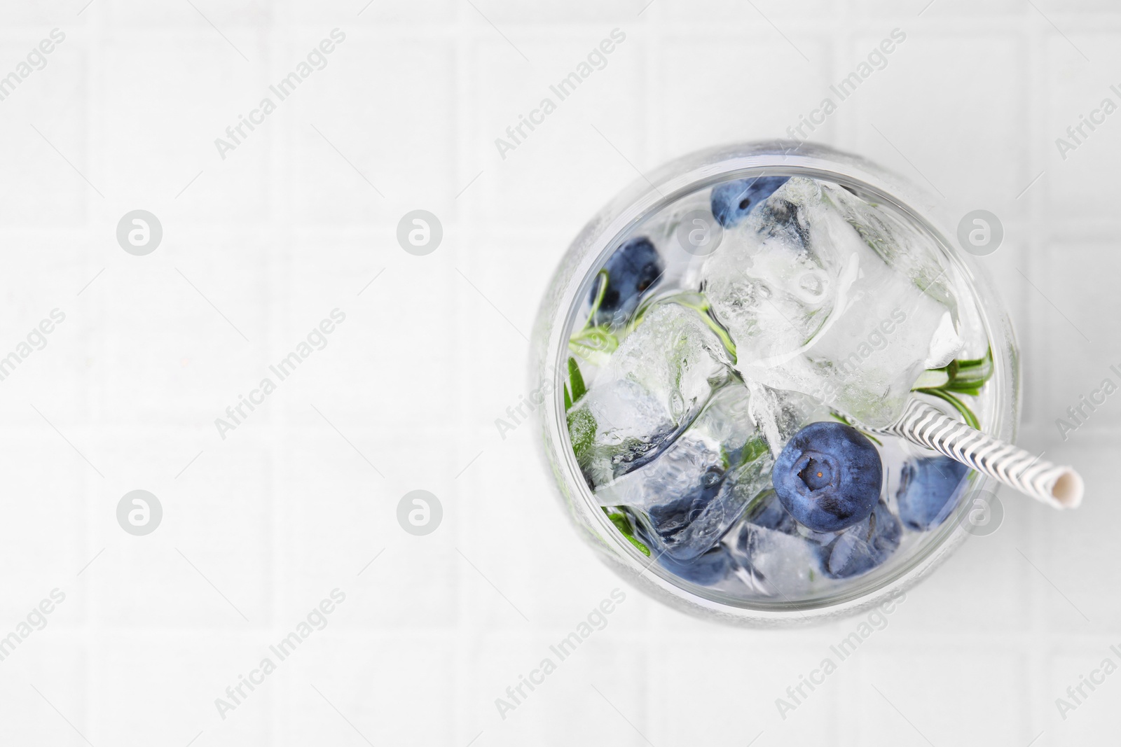 Photo of Refreshing water with blueberries and rosemary in glass on white tiled table, top view. Space for text