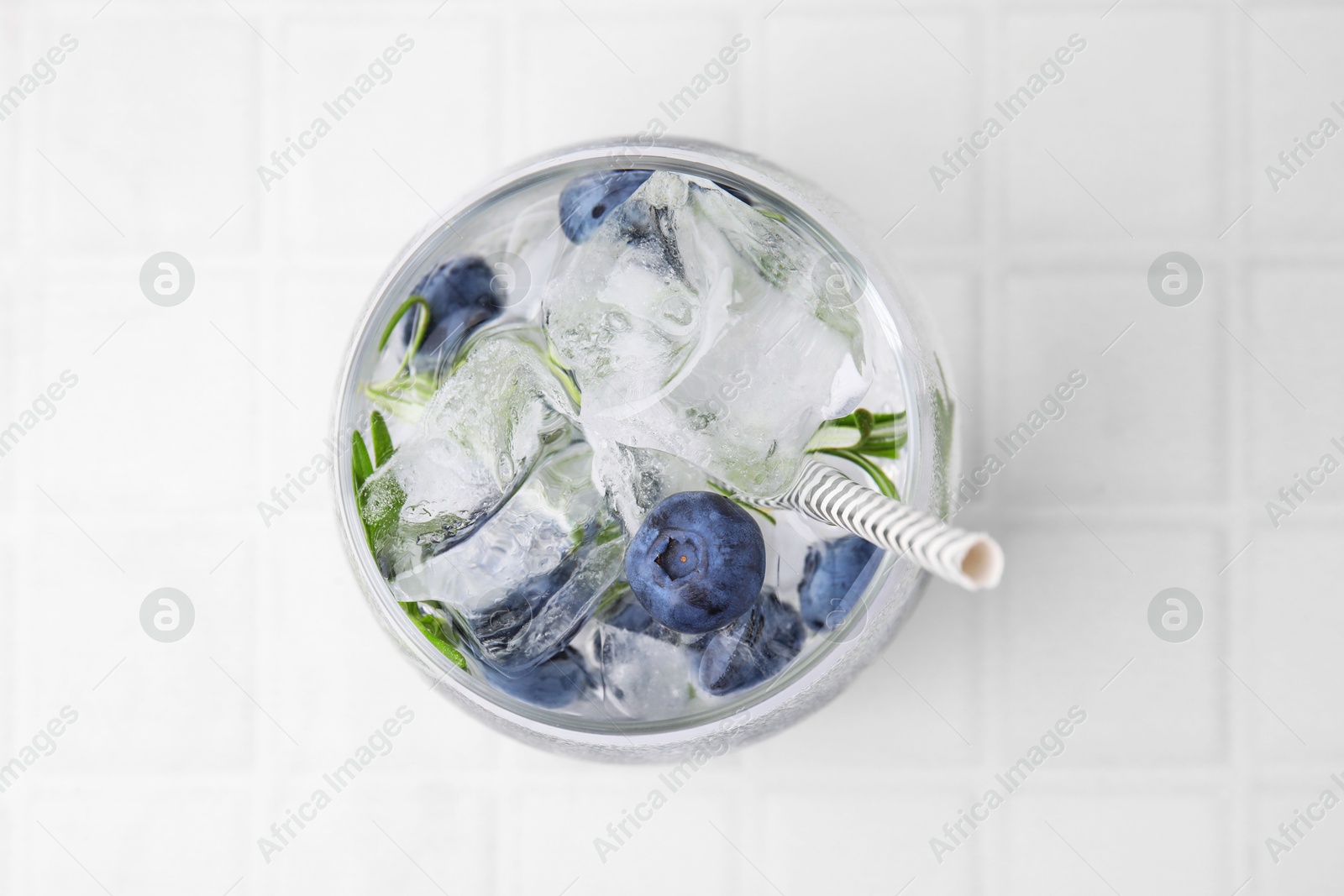 Photo of Refreshing water with blueberries and rosemary in glass on white tiled table, top view