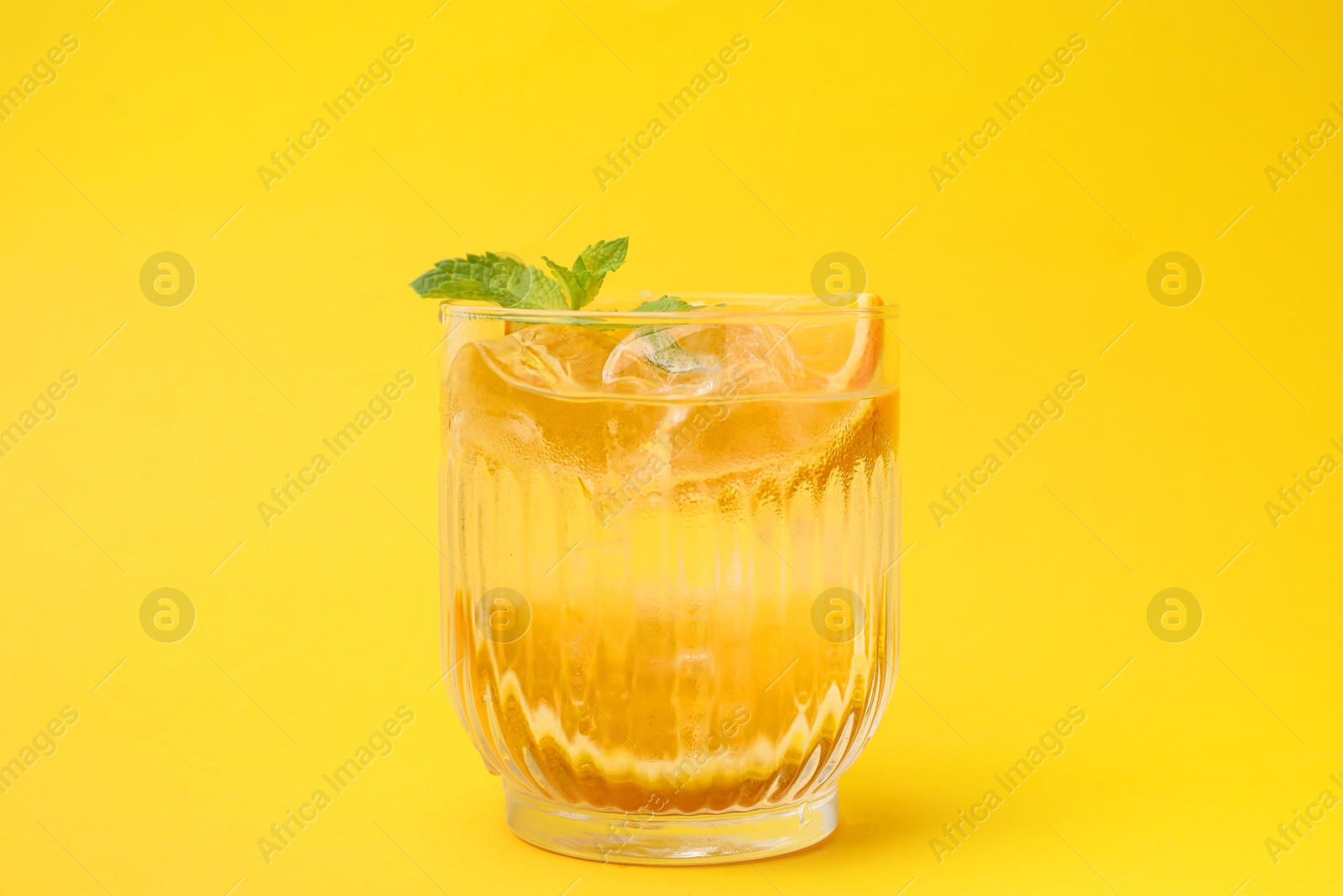 Photo of Refreshing water with orange and mint in glass on yellow background