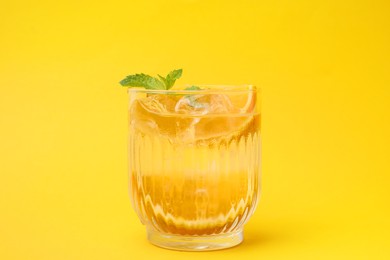 Photo of Refreshing water with orange and mint in glass on yellow background