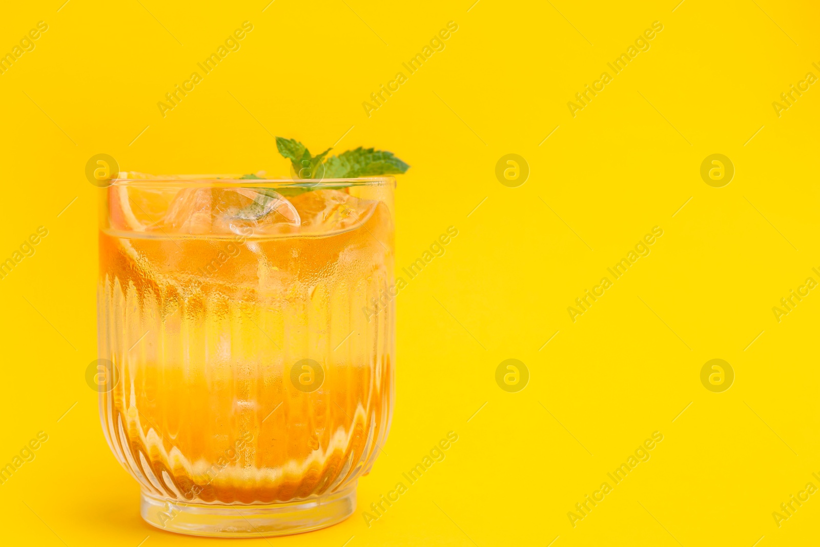 Photo of Refreshing water with orange and mint in glass on yellow background, space for text