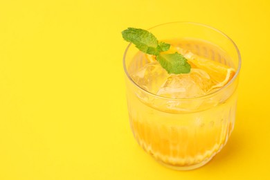 Photo of Refreshing water with orange and mint in glass on yellow background, closeup. Space for text