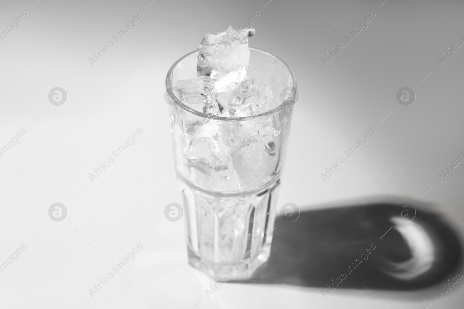 Photo of One glass with ice for refreshing drink on grey background, closeup