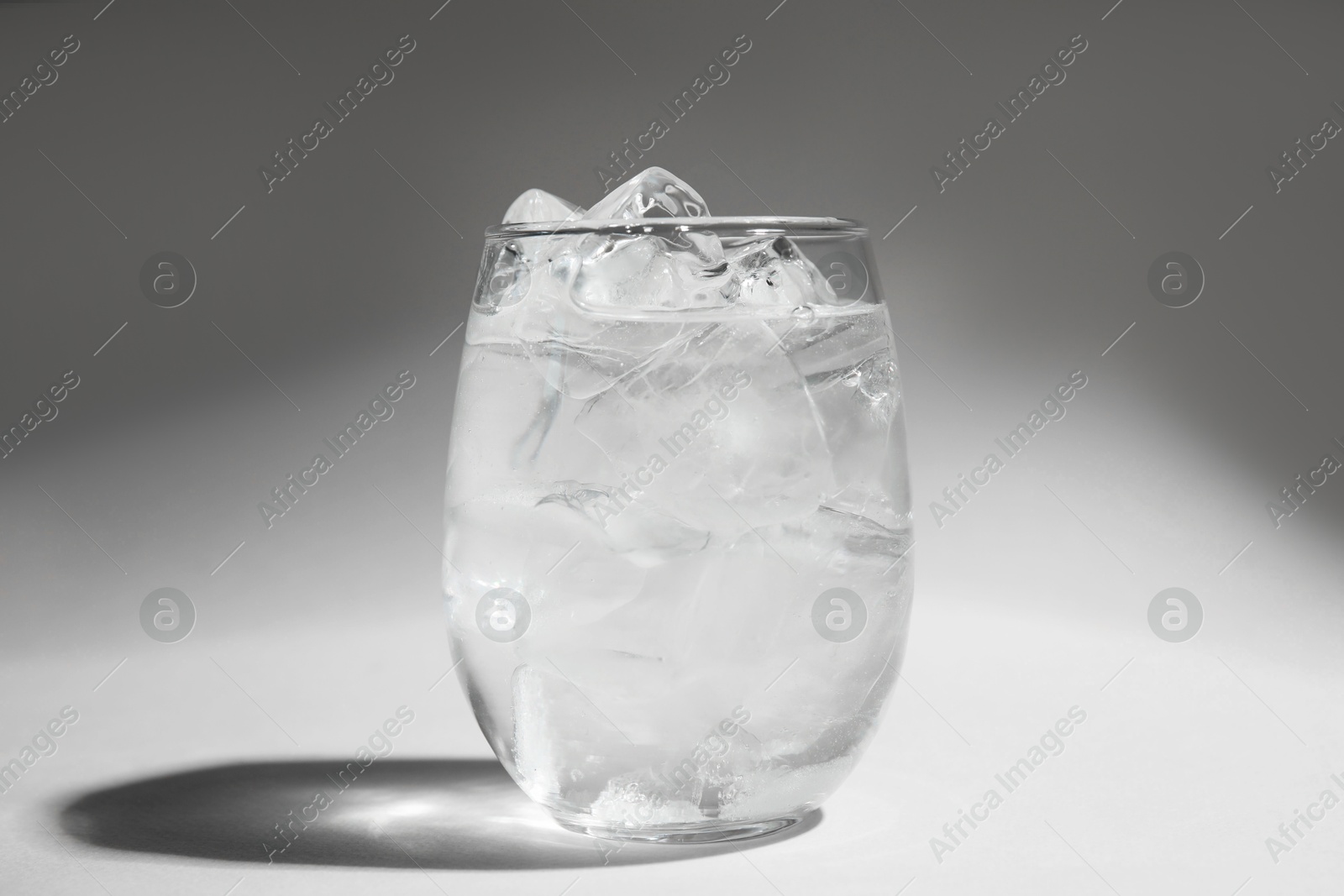 Photo of Refreshing water with ice in glass on grey background, closeup