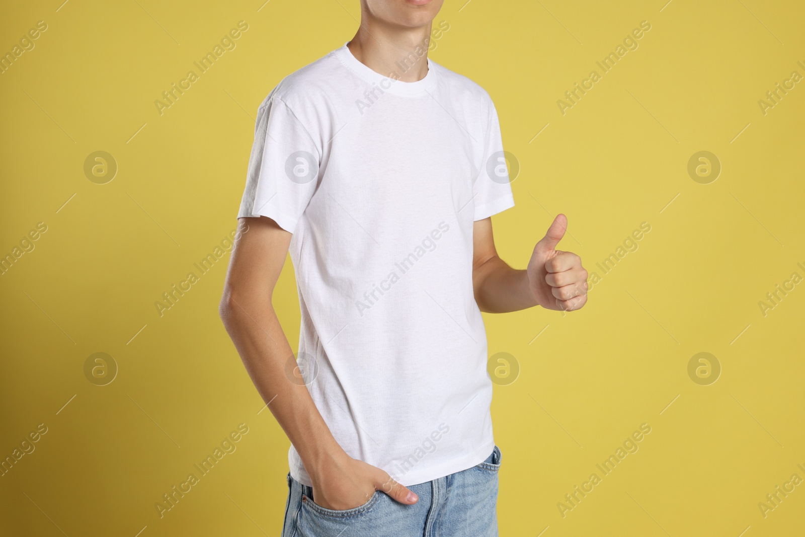 Photo of Teenage boy wearing white t-shirt and showing thumbs up on yellow background, closeup