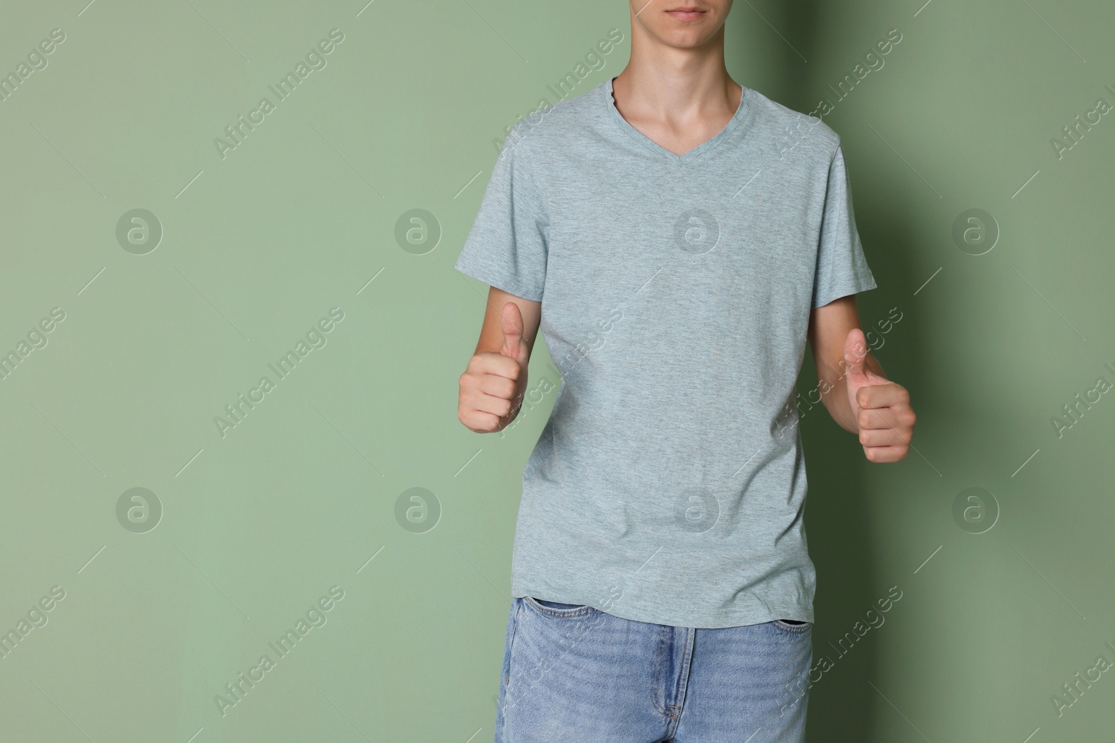 Photo of Teenage boy wearing light grey t-shirt and showing thumbs up on green background, closeup. Space for text