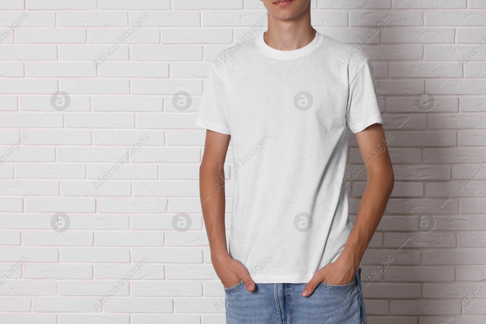 Photo of Teenage boy wearing t-shirt near white brick wall, closeup. Space for text