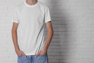 Photo of Teenage boy wearing t-shirt near white brick wall, closeup. Space for text