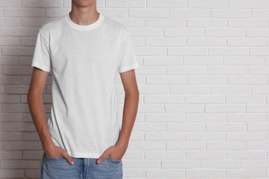 Photo of Teenage boy wearing t-shirt near white brick wall, closeup. Space for text