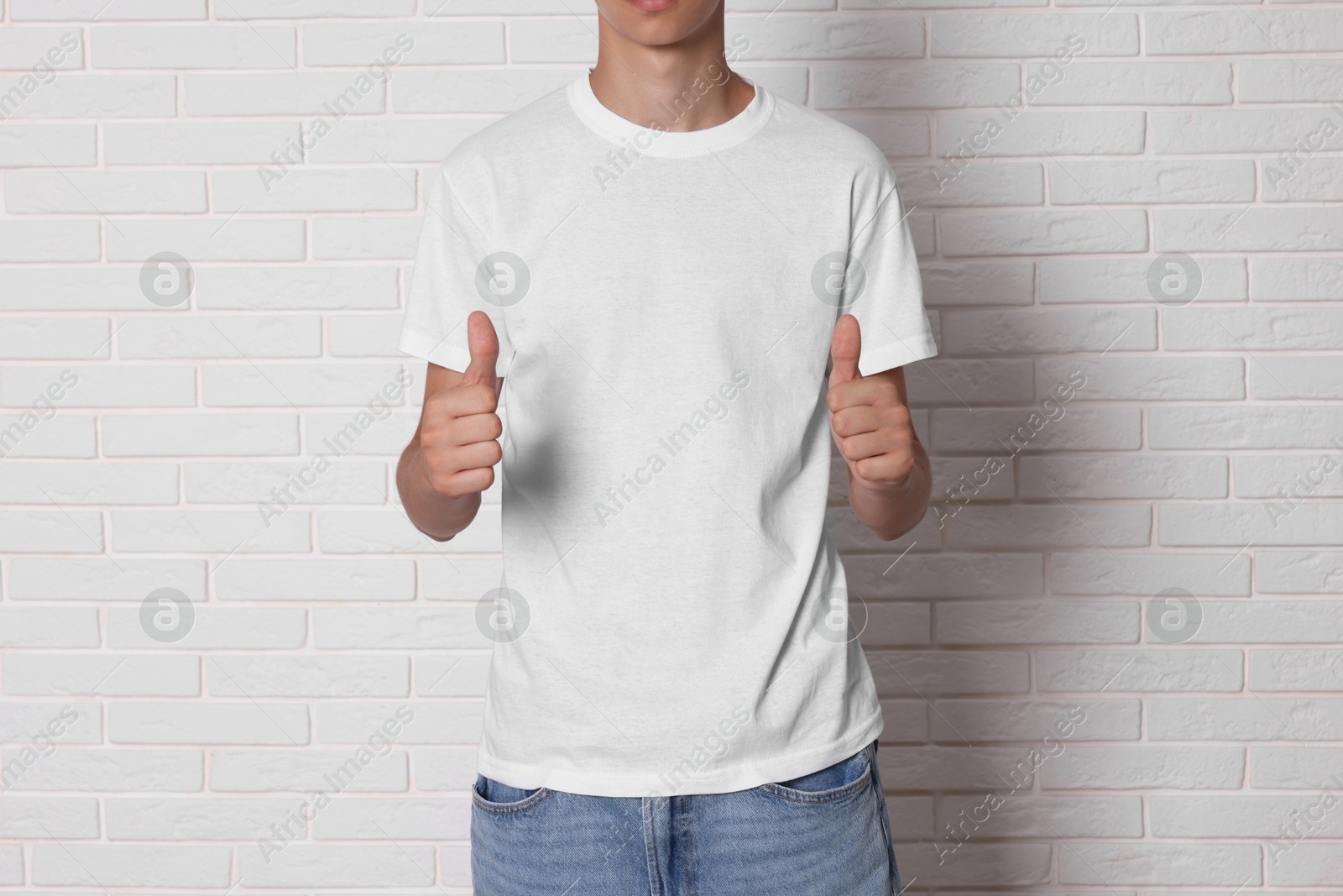 Photo of Teenage boy wearing t-shirt and showing thumbs up near white brick wall, closeup