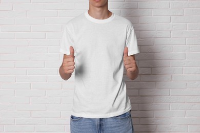 Photo of Teenage boy wearing t-shirt and showing thumbs up near white brick wall, closeup