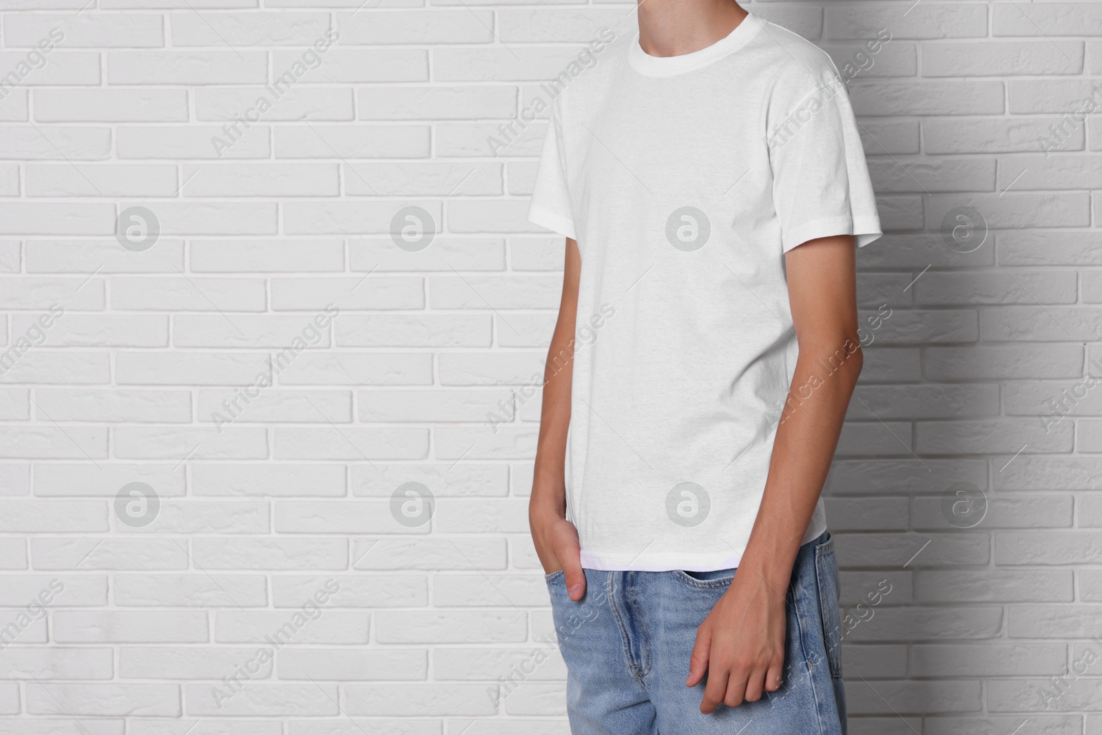 Photo of Teenage boy wearing t-shirt near white brick wall, closeup. Space for text