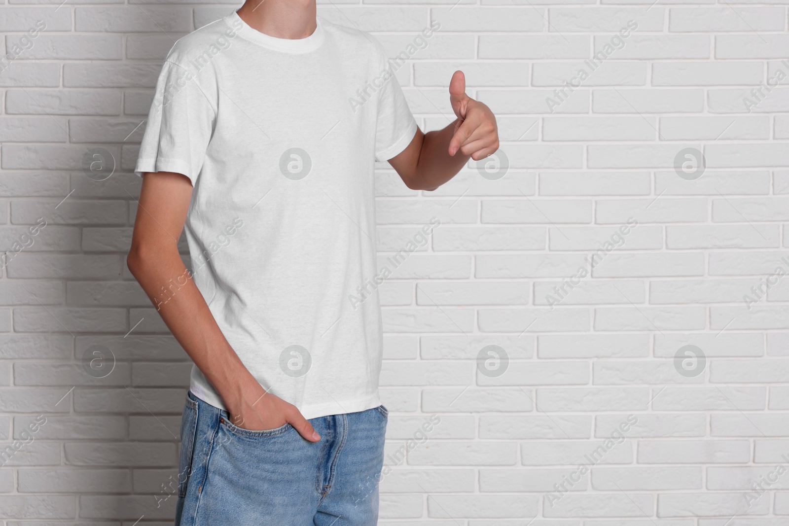 Photo of Teenage boy wearing t-shirt near white brick wall, closeup. Space for text