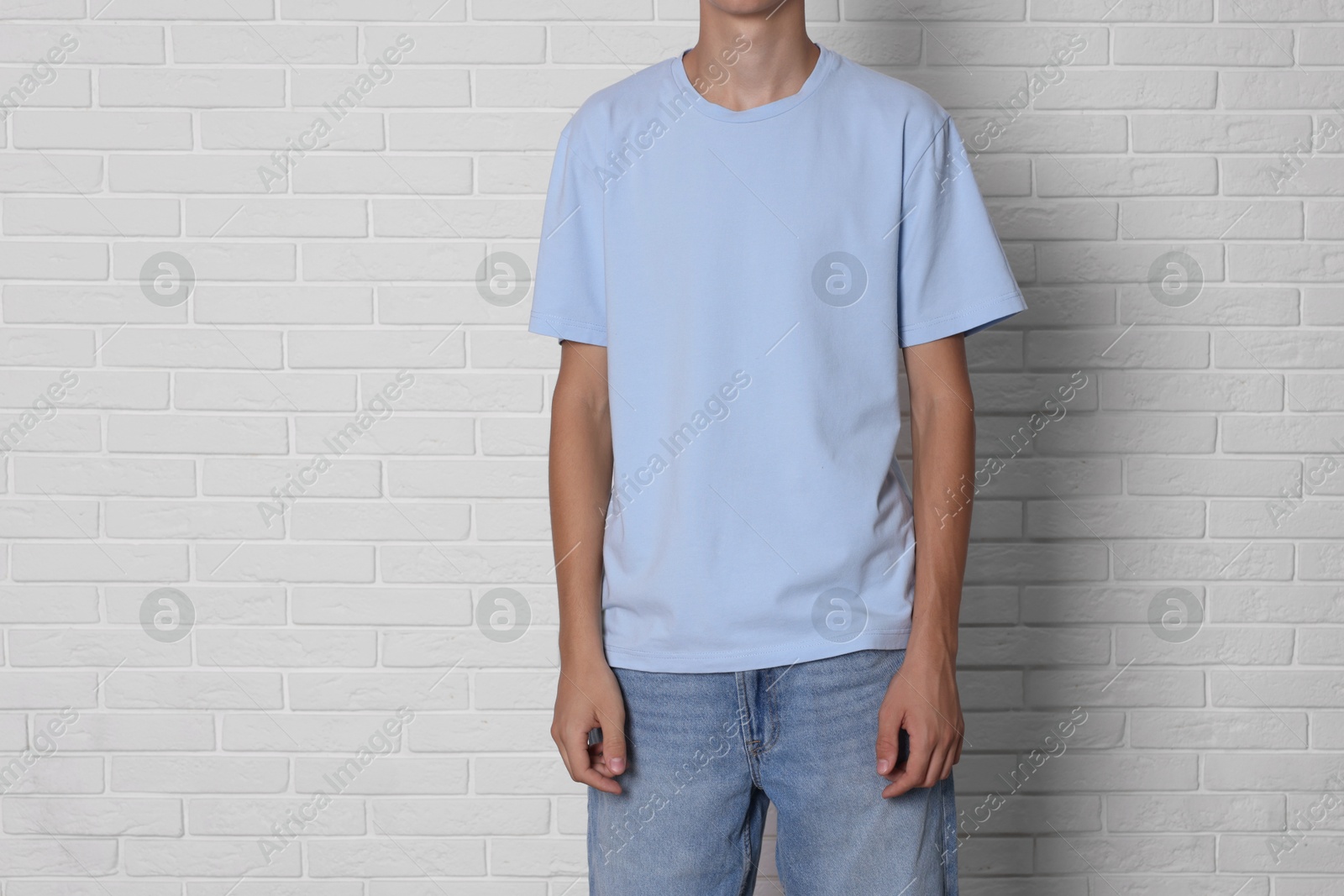 Photo of Teenage boy wearing light blue t-shirt near white brick wall, closeup. Space for text