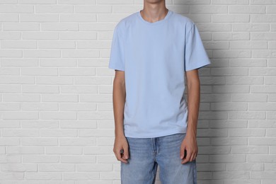 Photo of Teenage boy wearing light blue t-shirt near white brick wall, closeup. Space for text