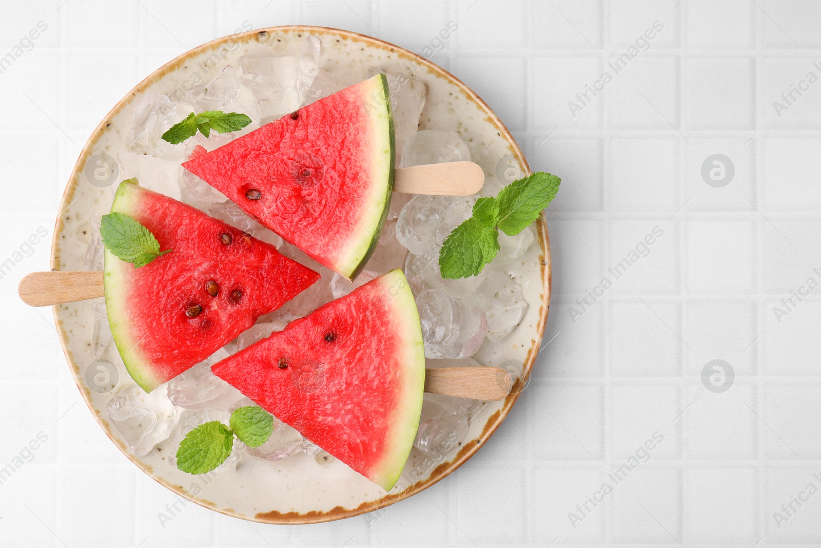 Photo of Pieces of tasty watermelon, ice cubes and mint on white tiled table, top view. Space for text