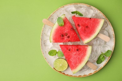 Photo of Pieces of tasty watermelon, ice cubes, lime and mint on green table, top view. Space for text