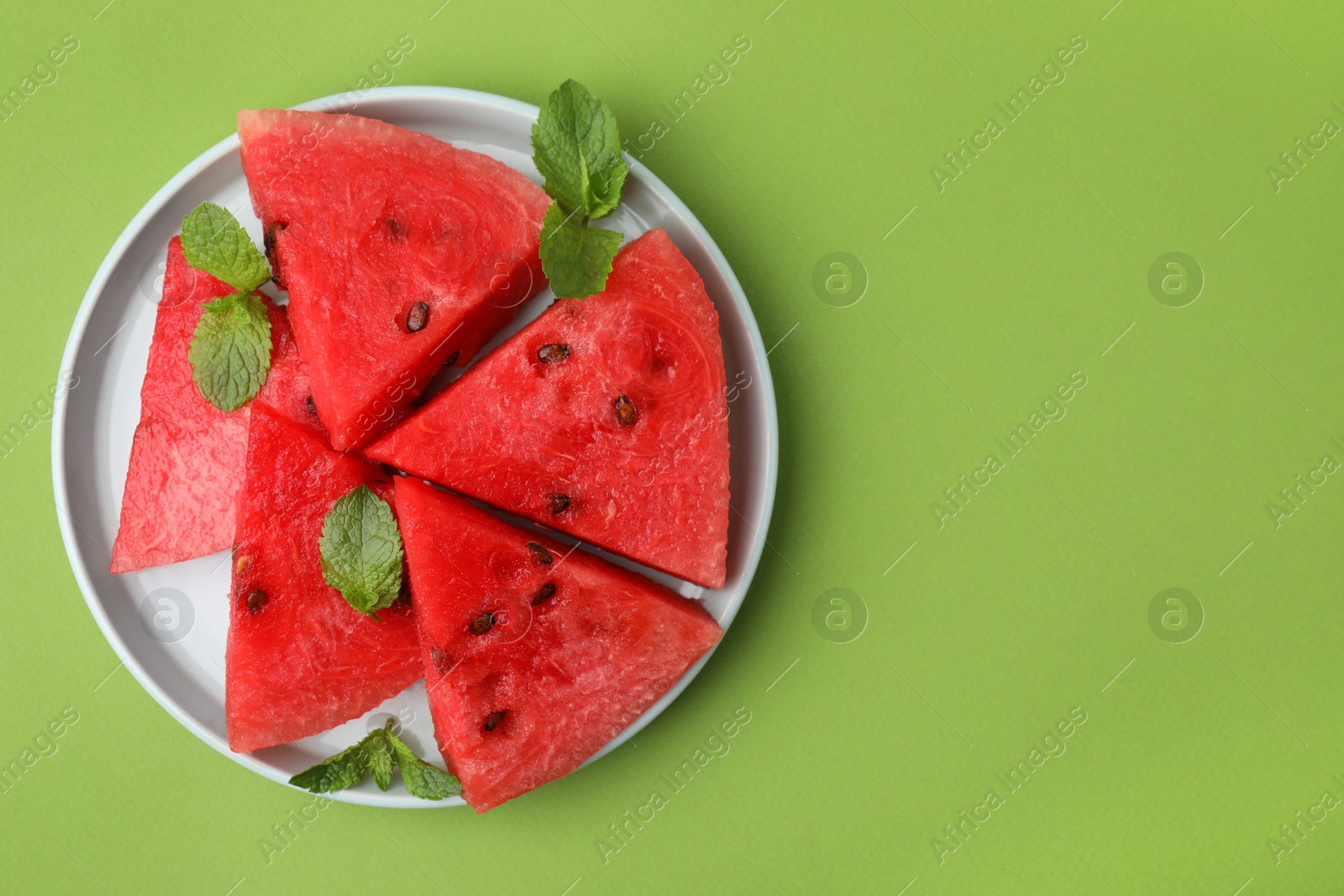 Photo of Pieces of tasty watermelon and mint on green table, top view. Space for text