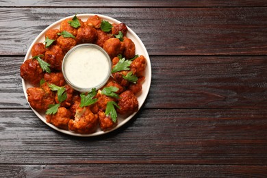 Photo of Baked cauliflower buffalo wings with parsley and sauce on wooden table, top view. Space for text