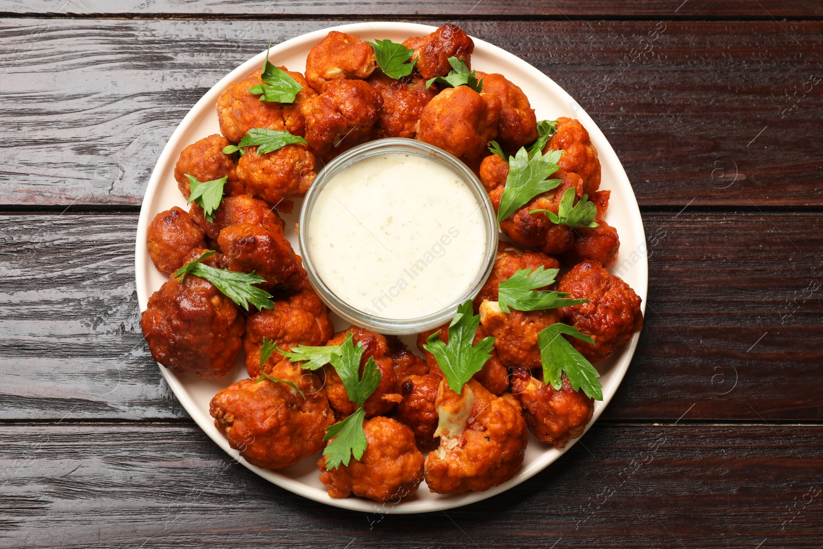 Photo of Baked cauliflower buffalo wings with parsley and sauce on wooden table, top view