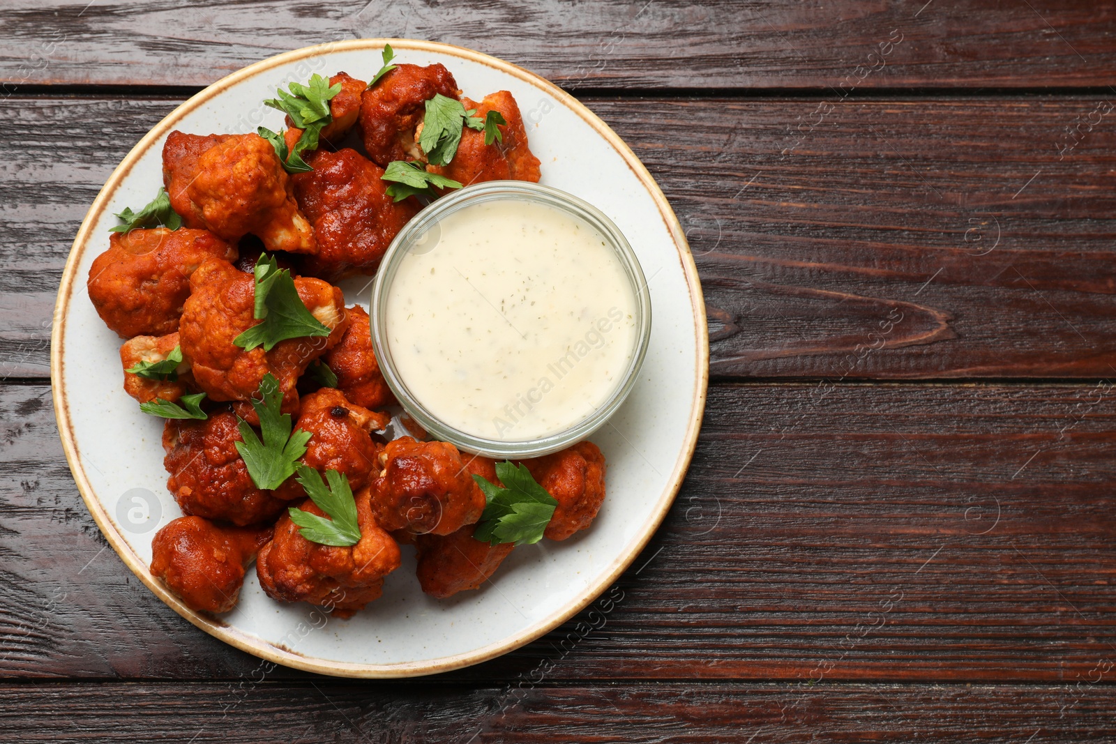 Photo of Baked cauliflower buffalo wings with parsley and sauce on wooden table, top view. Space for text