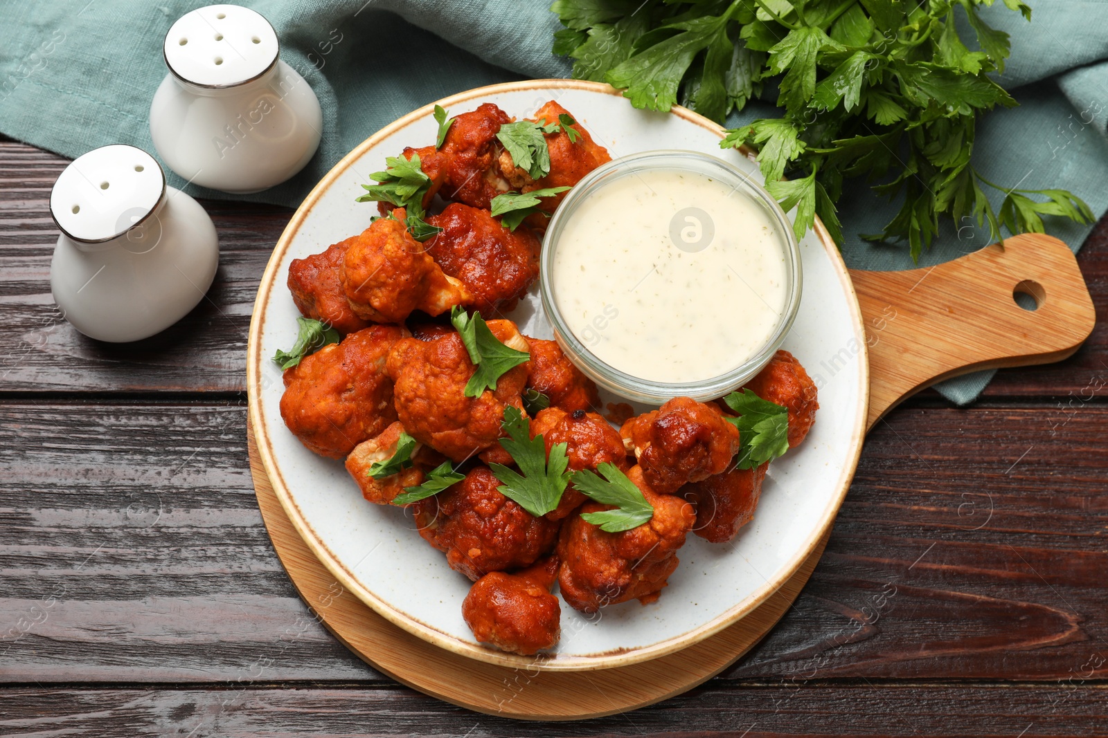 Photo of Baked cauliflower buffalo wings, parsley and sauce on wooden table, top view