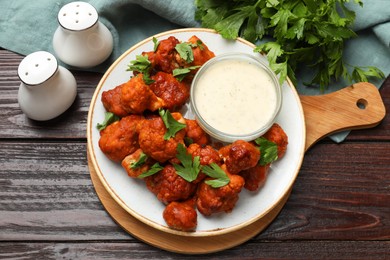 Photo of Baked cauliflower buffalo wings, parsley and sauce on wooden table, top view