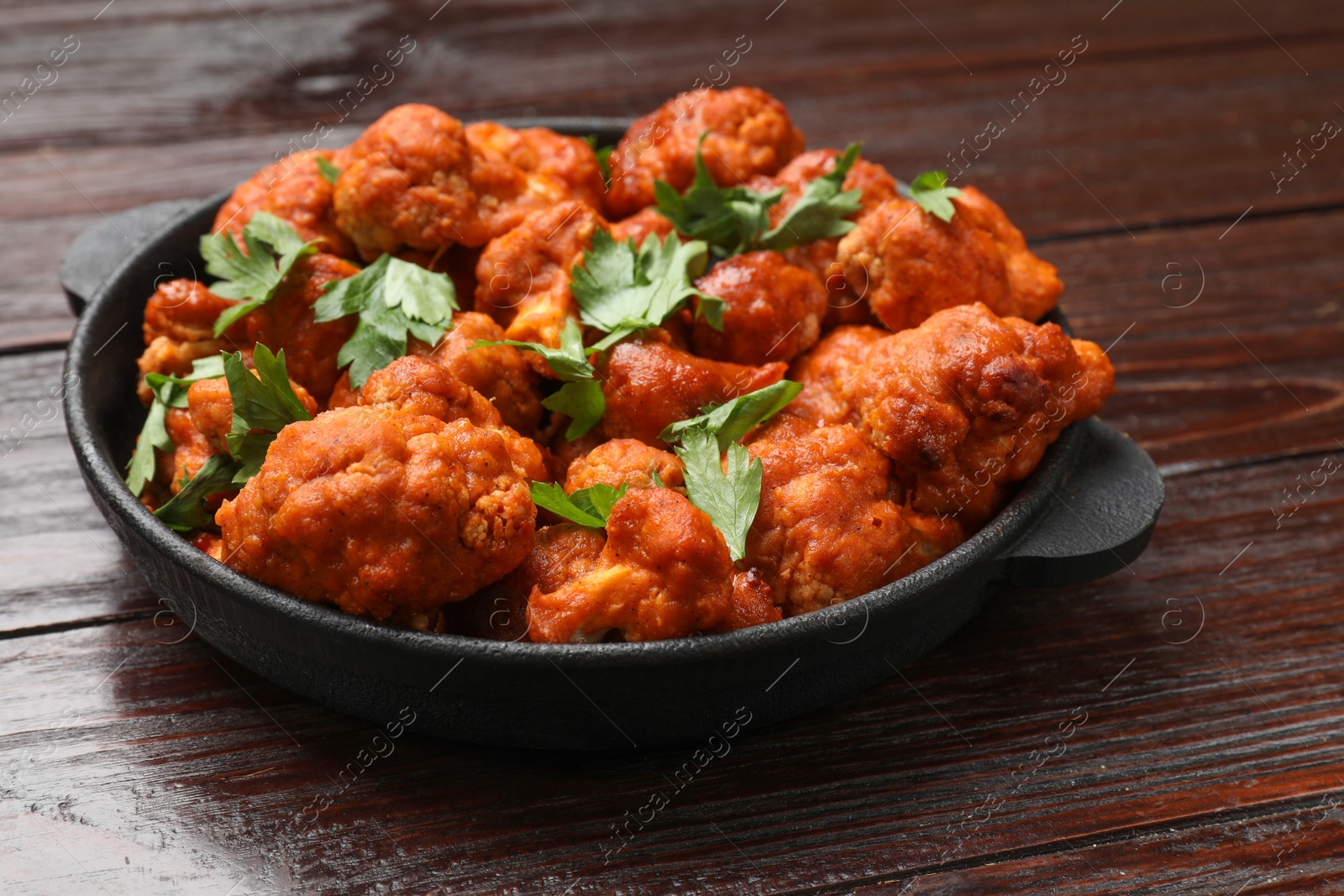 Photo of Baked cauliflower buffalo wings with parsley in baking dish on wooden table, closeup