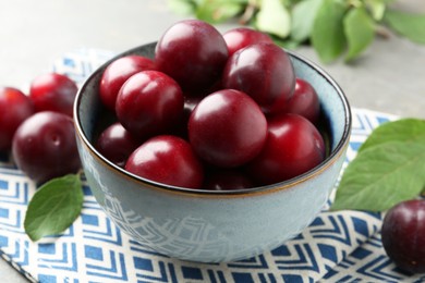 Photo of Tasty ripe plums in bowl on grey table, closeup