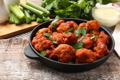 Photo of Baked cauliflower buffalo wings with parsley in baking dish on wooden table, closeup