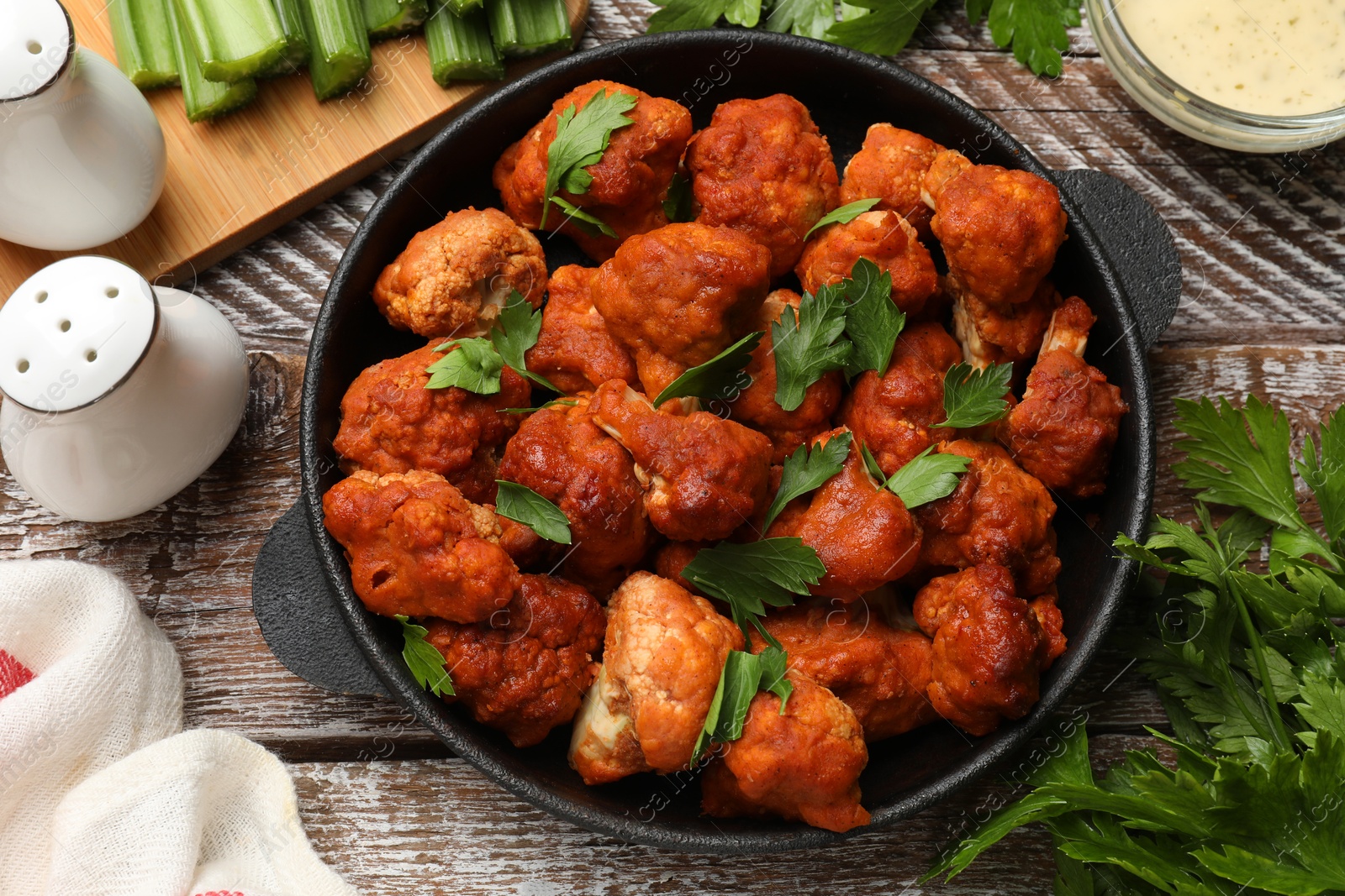 Photo of Baked cauliflower buffalo wings with parsley served on wooden table, flat lay