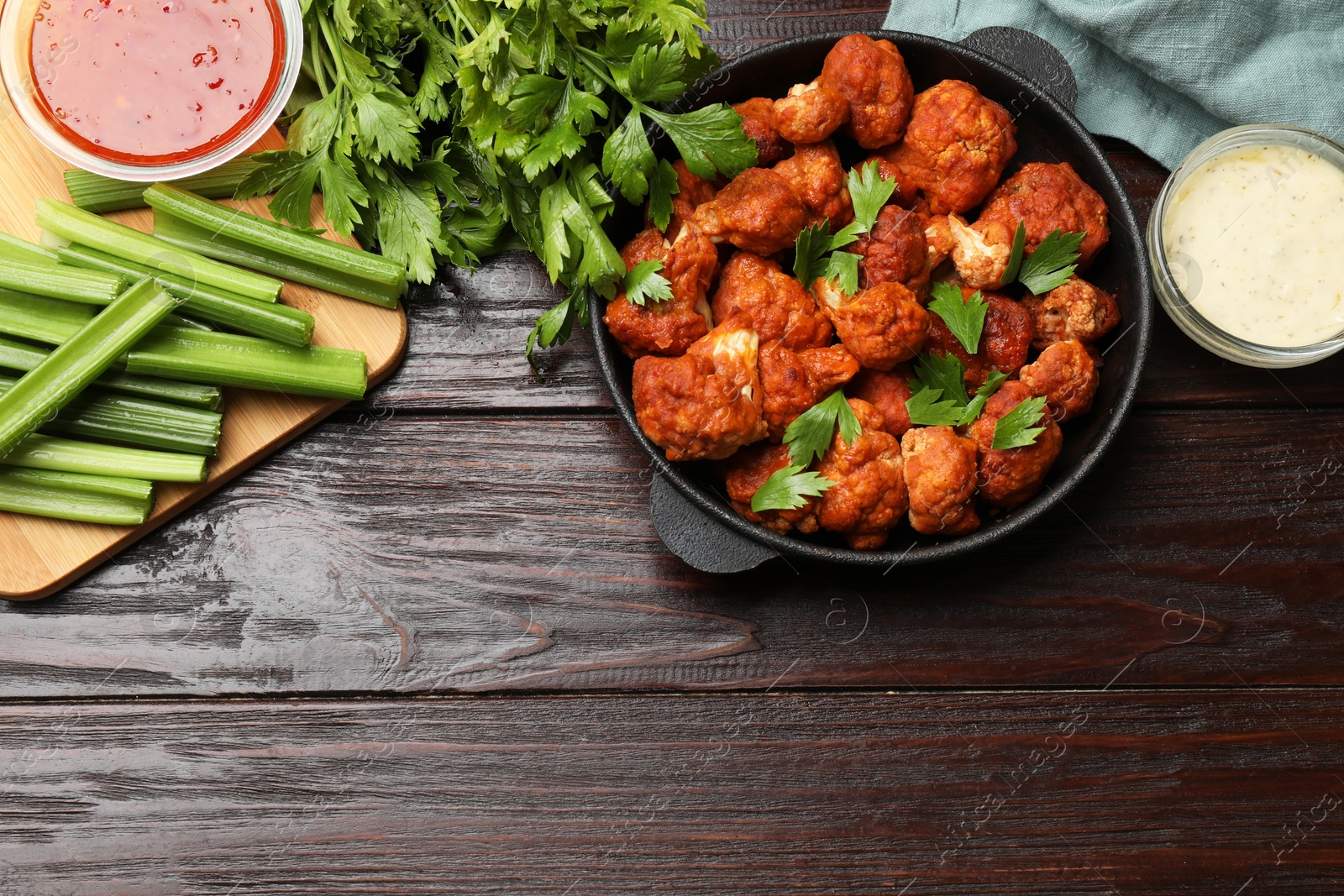 Photo of Tasty cauliflower buffalo wings, sauces and celery on wooden table, flat lay. Space for text