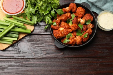 Photo of Tasty cauliflower buffalo wings, sauces and celery on wooden table, flat lay. Space for text