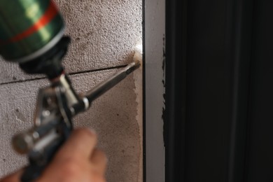 Repairman with polyurethane foam insulating new door at home, closeup