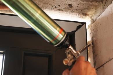 Photo of Repairman with polyurethane foam insulating new door at home, closeup