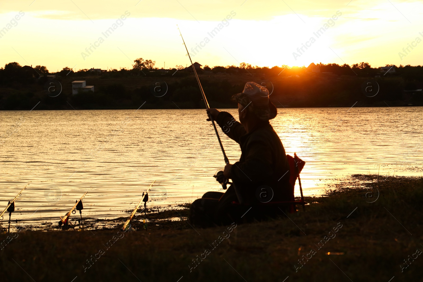 Photo of Fisherman with rod fishing near lake at sunset. Space for text