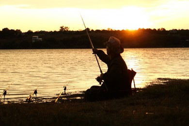 Fisherman with rod fishing near lake at sunset. Space for text