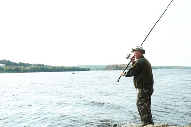 Photo of Fisherman with rod fishing near lake at summer, space for text