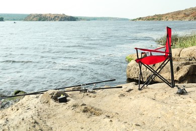 Chair and two fishing rods on shore near lake outdoors