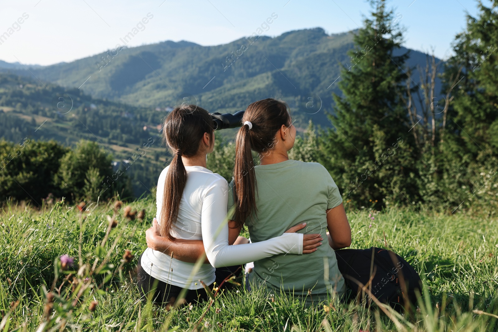 Photo of Women with binoculars on green grass in beautiful mountains, back view