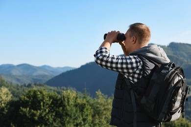 Photo of Man with backpack looking through binoculars in beautiful mountains, space for text