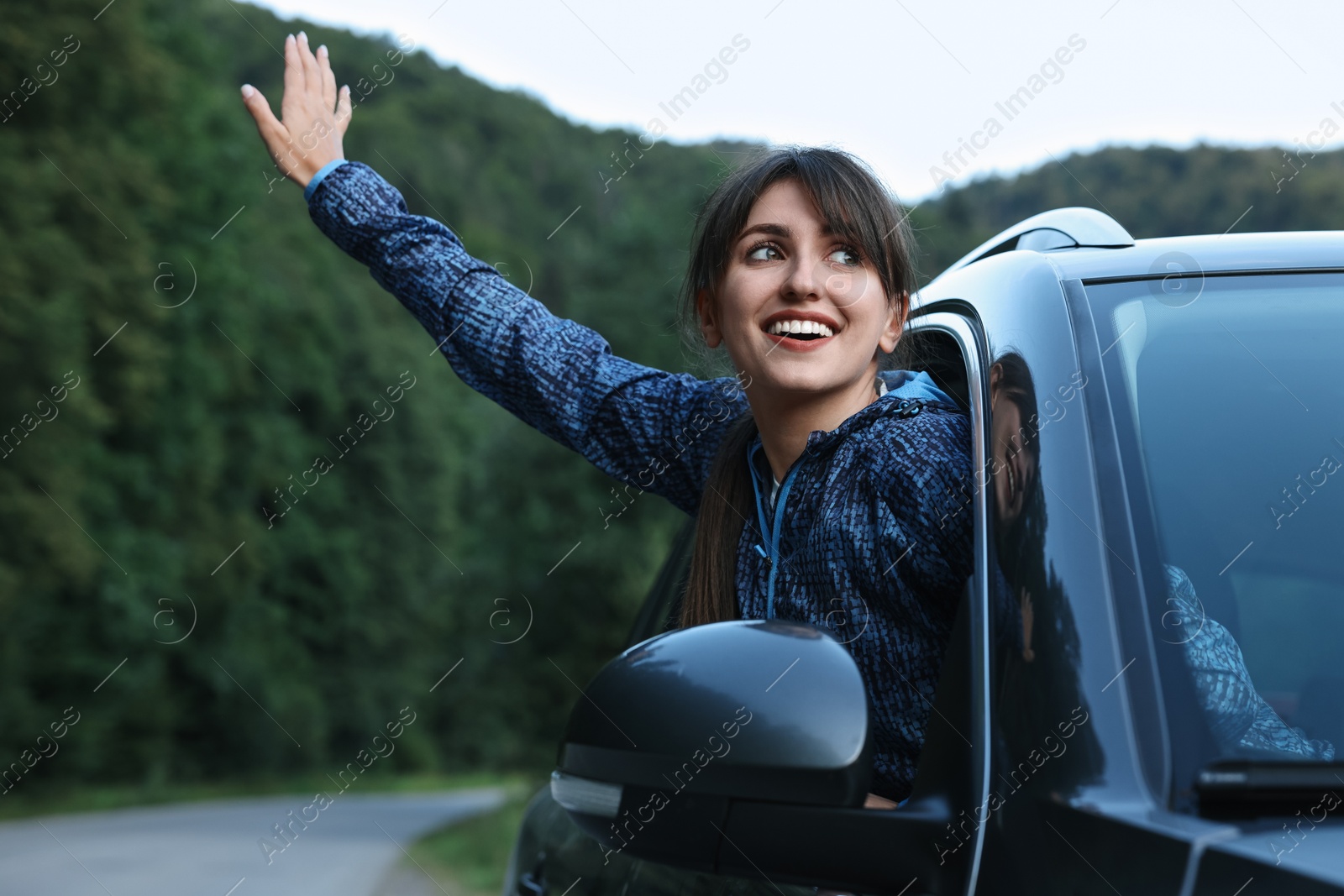 Photo of Smiling woman leaning out of car window in beautiful mountains